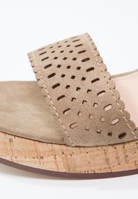 Sandale beige avec une sangle en daim perforé, des bords festonnés, une semelle semblable à du liège et un léger rembourrage pour le confort.