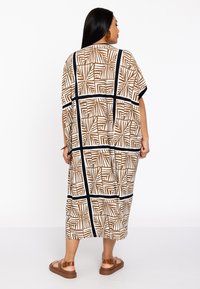 Robe de style kimono à motifs marron et blanc, coupe ample, manches courtes et accents noirs. Longueur jusqu'au sol et fabriquée en tissu léger.