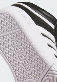 Černobílé tenisky Adidas částečně zobrazené, s texturovanou bílou gumovou podrážkou s diamantovým vzorem a vyraženým logem.