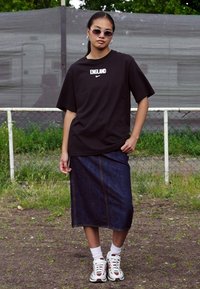 Black oversized T-shirt with "England" text, blue denim skirt, white athletic shoes, and sunglasses; shown against a grassy background.