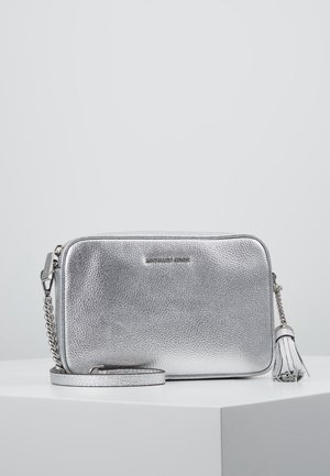 Zilverkleurige crossbodytas van gestructureerd leer met kettingriem en tassel detail, geplaatst op een wit oppervlak tegen een neutrale achtergrond.