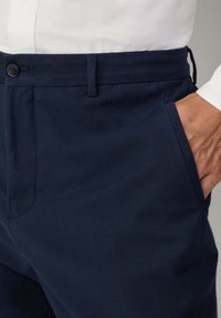 Pantalon bleu marine en tissu texturé, avec fermeture à bouton, poches latérales et une coupe ajustée avec passants de ceinture.