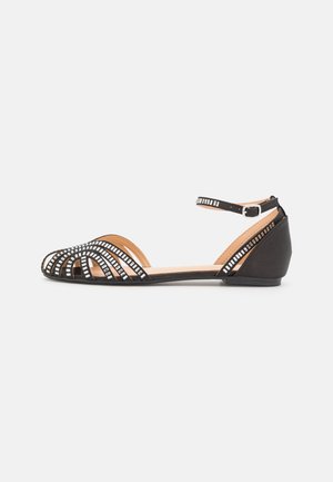 Sandale plate noire avec bout ouvert, boucle à la bride de cheville et clous carrés argentés décoratifs sur les lanières.