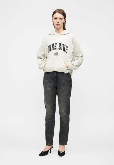 Woman wearing light gray hoodie with "NINE BING SPORT" text, dark gray jeans, and black pointed heels, standing against a plain white background.
