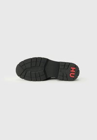 Black rubber shoe sole with textured tread pattern. Features a red "HU" logo on the heel. Smooth surface with defined grip areas.