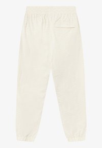 Joggers de couleur crème claire avec une taille élastique, des chevilles resserrées et une poche arrière unique, dotée de détails en relief subtils.