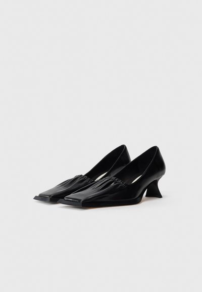 Black leather heels with a square toe and a unique angular heel. Features gathered texture at the opening and smooth surface.