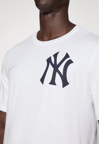 White cotton t-shirt featuring a large black New York Yankees logo on the chest and a small gray Nike swoosh on the left sleeve.