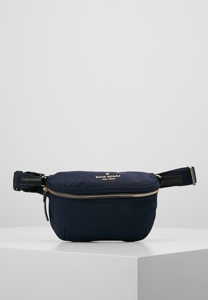 Banane bleu marine Kate Spade New York avec fermeture éclair dorée et sangle réglable sur un piédestal blanc sur fond gris.