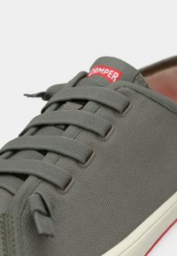 Γκρι καμβάς αθλητικό παπούτσι με στρογγυλεμένη μύτη, επίπεδα κορδόνια και κόκκινο λογότυπο "Camper". Εξώφυλλο από καουτσούκ με λευκές και κόκκινες λεπτομέρειες. Υπόδημα με υφή στην επιφάνεια.