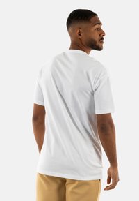 Camiseta blanca de algodón con cuello redondo clásico, mangas cortas y un ajuste relajado. Presenta una textura suave y sin gráficos ni patrones visibles.