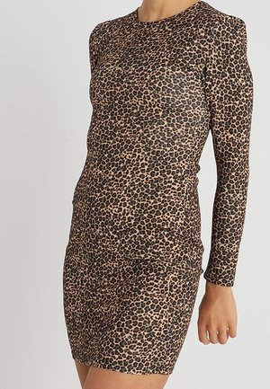 Femme portant une robe ajustée à manches longues et longueur genou, avec un imprimé léopard brun et noir.