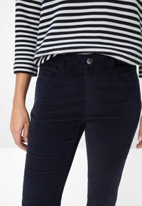 Navy corduroy broek met knoopsluiting, zijzakken en verticale ribbels, gecombineerd met een gestreepte langwerpige top.