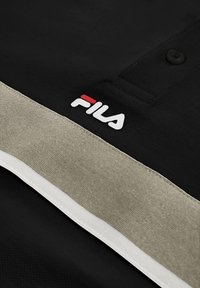Tissu noir avec des rayures beige et blanches et un logo FILA en blanc et rouge près d'un col boutonné.