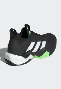 Chaussure de sport noire avec des rayures blanches, dotée d'un dessus texturé, de accents verts et d'un design de semelle distinct en noir et blanc.