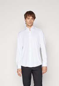 Camicia bianca a maniche lunghe con colletto button-down, texture liscia e polsini azzurri, indossata con pantaloni scuri. Nessun motivo o accento visibile.