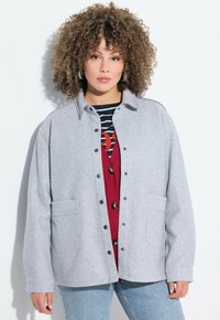 Grijze, fleece knoopjack met twee voorzakken en een kraag. Draag het over een rode gestreepte top met metalen drukknoopknopen.
