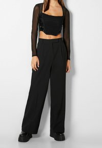Top corto nero con texture arricciata e maniche lunghe trasparenti, abbinato a pantaloni neri a vita alta e gamba larga e scarpe con plateau spesse.