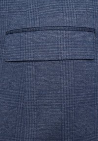 Niebieska tkanina w kratę o gładkiej fakturze. Wyposażona w jedną poziomą kieszeń z kontrastowym ciemnym wykończeniem. Wzory są subtelne i jednorodne.