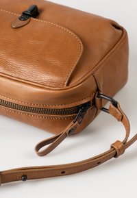 Brown leather crossbody bag with a textured finish, zipper closure, adjustable strap, and minimalist design details.