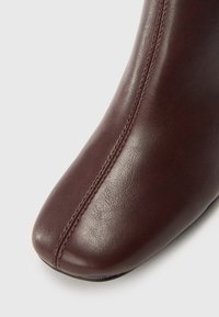 Bottine en cuir bordeaux avec une texture lisse, un bout pointu et des détails de couture visibles sur le côté. La couture centrale ajoute de la structure.