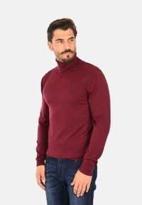 Maglione a collo alto color bordeaux realizzato in un materiale morbido e liscio. Presenta maniche lunghe e polsini a costine, abbinato a jeans in denim blu.