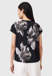 Camiseta negra con gran estampado floral gris en la parte de atrás, con mangas cortas enrolladas y un diseño de corte holgado.