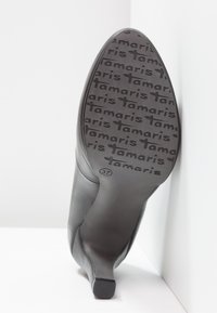 Semelle d'une chaussure noire à talons hauts tournée vers la caméra, avec le nom de la marque "Tamaris" et la taille "37" en relief sur la semelle.