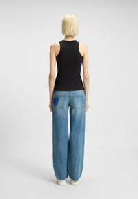 Top senza maniche nera abbinato a jeans a gamba larga di un blu chiaro con una grafica di faccina sorridente blu sulla tasca posteriore destra.