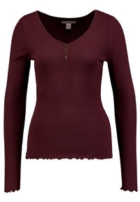 Långärmad, ribbad vinröd topp med V-ringning, tre knappar under halsringningen och ett salladskantat avslut på ärmar och nederdel.