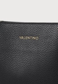 Sac à main en cuir noir avec une surface texturée, affichant un logo "VALENTINO" en relief de couleur dorée à l'avant.