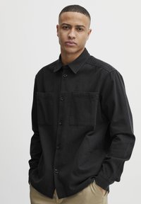 Zwarte button-up shirt van stof, met twee voorkanten pockets, een kraag en lange mouwen. Geweven afwerking met een relaxte pasvorm.