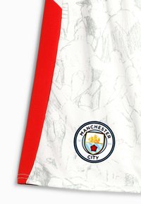 Hvid sportsjersey med røde detaljer, prydet med grafisk design og Manchester City-logoet nederst til venstre. Åndbart materiale.