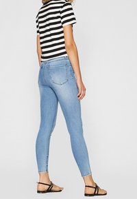 Jeans ajustados de color azul claro con una textura de denim suave, que cuentan con bolsillos traseros clásicos y un dobladillo limpio. Acompañados de una blusa a rayas en blanco y negro.