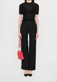 Czarny prążkowany top z krótkim rękawem w połączeniu z czarnymi, wysokim stanem spodniami; trzyma małą czerwoną torebkę z łańcuszkowym akcentem; czarne, spiczaste buty.