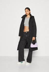 Cappotto lungo trapuntato nero con cappuccio, top grigio corto, jeans neri a gamba larga e una piccola borsa lilla. Presenta scarpe da ginnastica bianche.