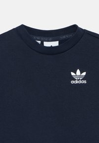 Φούτερ από βαμβάκι σε ναυτικό μπλε, με στρογγυλή λαιμόκοψη και λευκό κεντημένο λογότυπο Adidas στο αριστερό στήθος. Λείο ύφασμα και απλός σχεδιασμός.