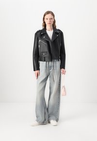 Black cropped leather biker jacket with silver zippers, paired with oversized light wash jeans and white sneakers, holding a small pink handbag.