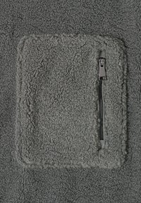 Tela de forro gris con una superficie texturizada, que presenta un bolsillo externo y un detalle de cremallera negra en el lateral.