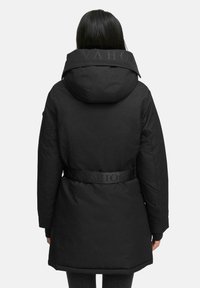 Parka nera con cappuccio, caratterizzata da un colletto testurizzato e una vita cintrata. Tessuto liscio, maniche lunghe e taglio fino al ginocchio. Dettagli del logo sulla cintura.