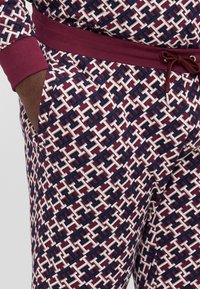 Bordeaux gemusterde joggers met witte en donkerblauwe geometrische designs. Kenmerken zijn een zachte textuur, een elastische tailleband en zijzakken.