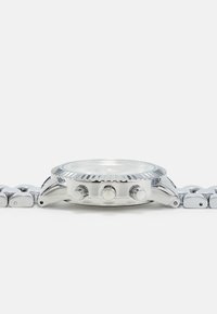 Silverfärgad kronografklocka med en rund, texturerad bezel, tre knappar på sidan och ett länkad metallarmbandsdesign. Klar glasfront.