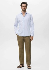 Helles blaues Langarmhemd mit Knopfverschluss, kombiniert mit khakifarbenen Hosen und schwarzen Sandalen. Glattes Material und lässige Passform.