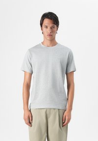 Grå bomulls t-skjorte med rund hals og korte ermer, med en subtil logo på brystet, sammen med lysebeige shorts.