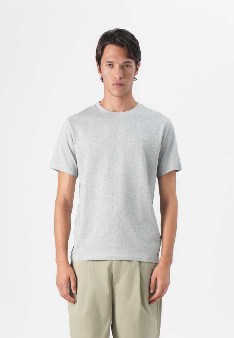 Grå bomulls t-skjorte med rund hals og korte ermer, med en subtil logo på brystet, sammen med lysebeige shorts.