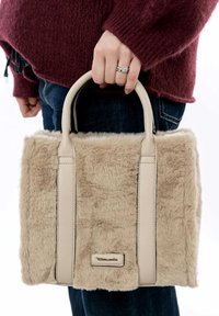 Beige faux fur handbag with smooth leather handles, rectangular shape, textured surface, and a small metallic logo plate on the front.
