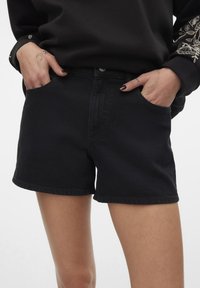 Svarta denimshorts med en figursydd design, som har framfickor, en jämn yta och en rå fåll vid benen.