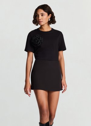 Abito t-shirt nero a maniche corte con una forma aderente e un dettaglio di rosa 3D nera sul petto. Tessuto liscio con una texture uniforme.