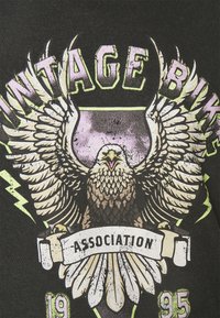 Camiseta negra con un diseño gráfico de un águila y rayos. Presenta el texto "BICIS VINTAGE" y "ASOCIACIÓN", con un aspecto desgastado.
