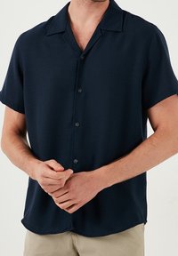 Ciemnogranatowa koszula na krótki rękaw z kołnierzykiem typu point, wykonana z lekkiego materiału, o luźnym kroju i subtelnym połysku.